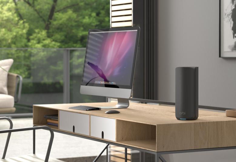 Sort NETGEAR Orbi RBE870B-satellit – placeret ved en computer på et skrivebord