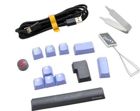 An assortment of keyboard accessories including a Ducky Cherry Silent Red USB cable, blue keycaps, a keycap puller, and a Ducky branded wrist rest, all set against a transparent background.