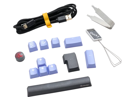 Various computer keyboard accessories on a transparent background, including keycaps, a cable, a keycap puller, and a spacebar for the Ducky One 3 - Classic Black / White Nordic - Fullsize - Cherry Silver, all displaying the "Ducky" brand.