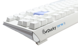 A close-up of a white mechanical keyboard, featuring PBT keycaps and the "Ducky" brand visible on the front side, set against a plain, light gray background.