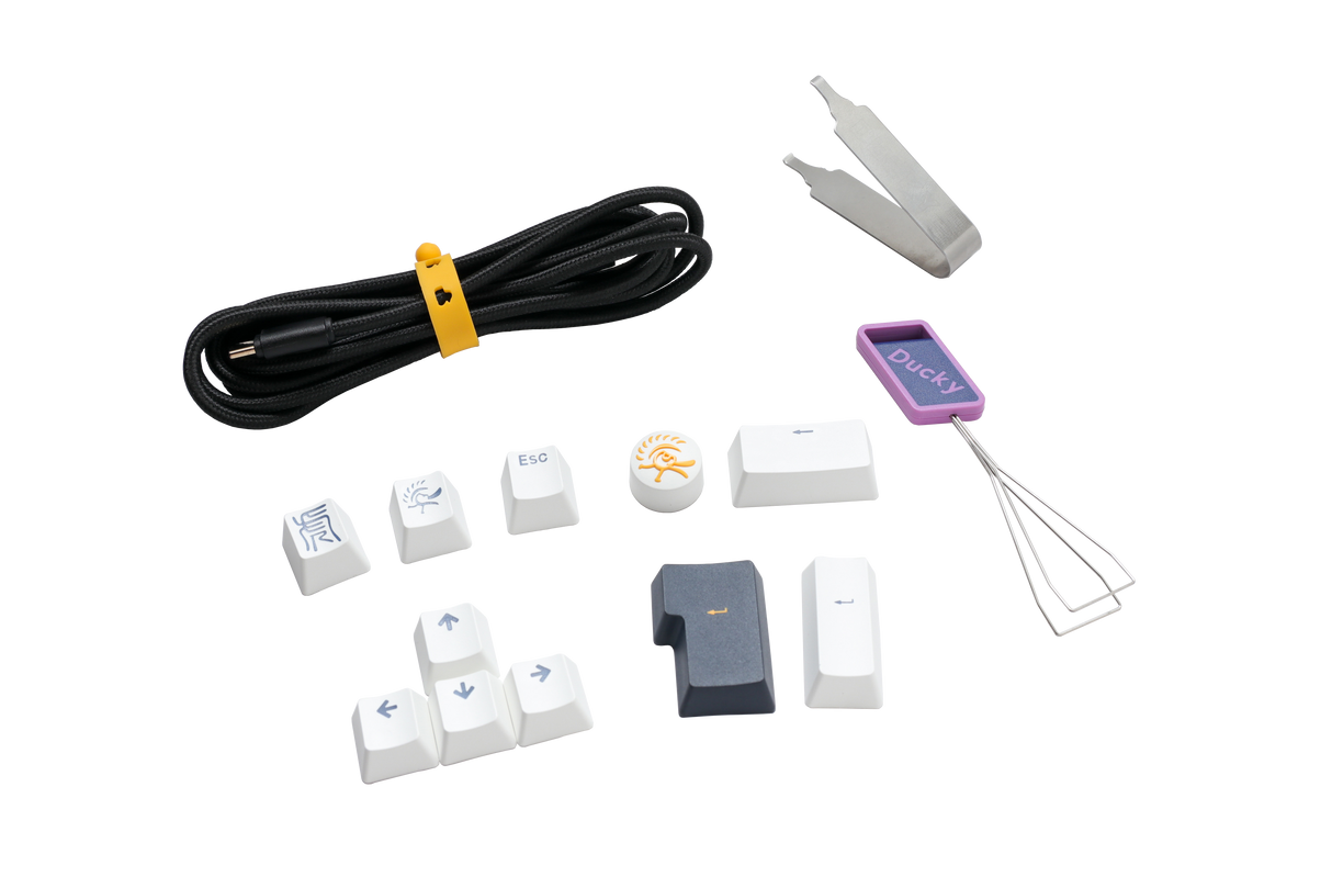 An assortment of Ducky keyboard accessories including a keycap puller, various PBT keycaps with symbols, a coiled cable, and additional small tools, all displayed on a white background.