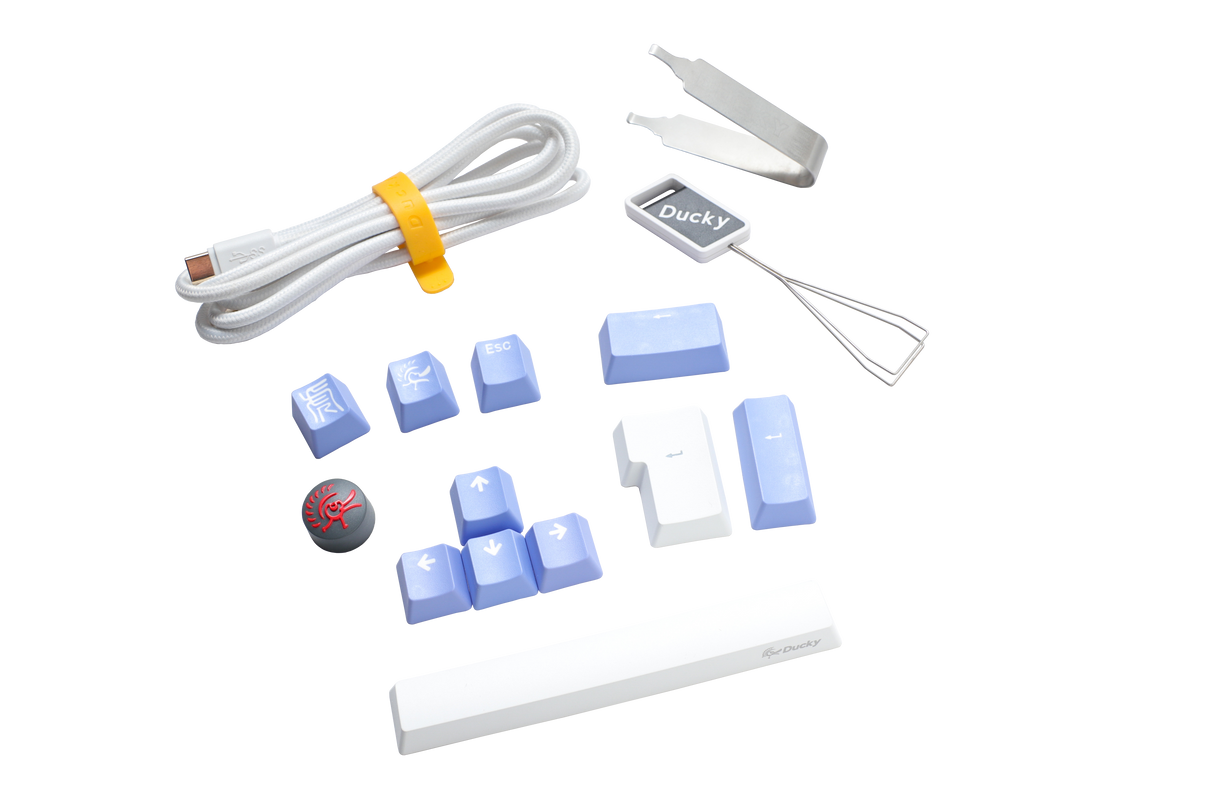 Assorted computer keyboard accessories including a white USB cable, a Ducky branded wire keycap puller, blue PBT keycaps, a red Cherry MX key switch, and silicone stabilizers.