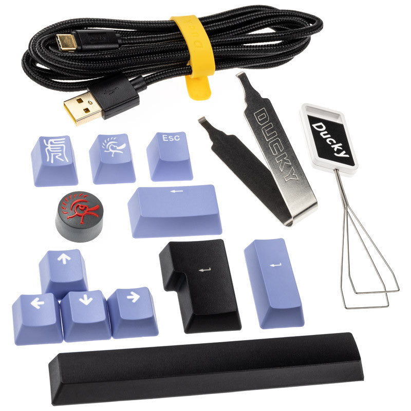 Variety of keyboard accessories including Ducky One 3 - Classic Black / White Nordic - TKL - Cherry Blue keycaps in shades of gray and blue, a yellow-banded USB cable, a wire keycap puller, and an "esc" tool